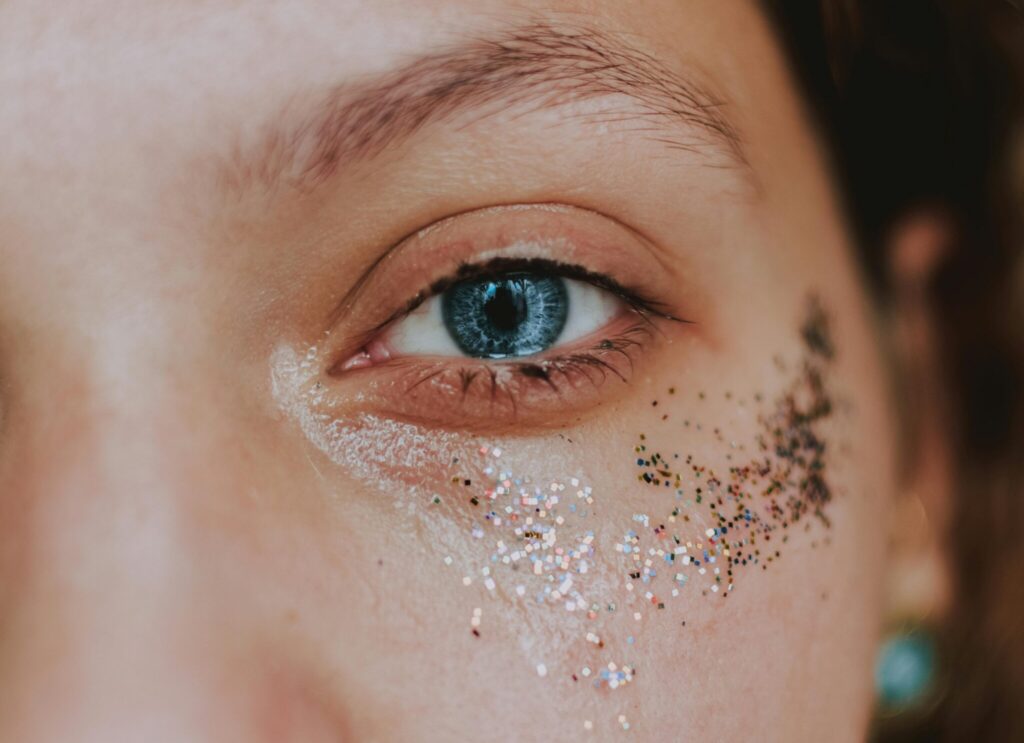 Closeup of crop anonymous young female with piercing and shiny glitters on face looking at camera in daylight