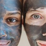 Crop cheerful multiethnic ladies with clay mask applied on faces looking at camera