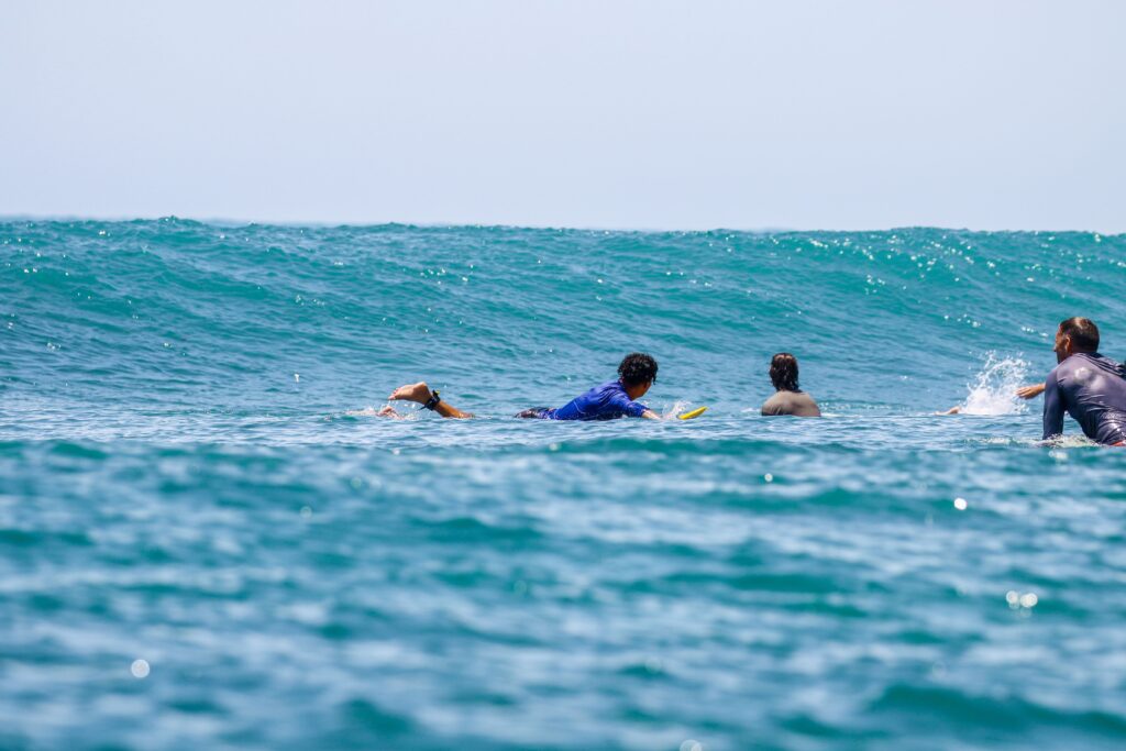 pexels-photo-15875334-15875334 Four surfers paddling on surfboards, preparing for an ocean wave on a sunny day.